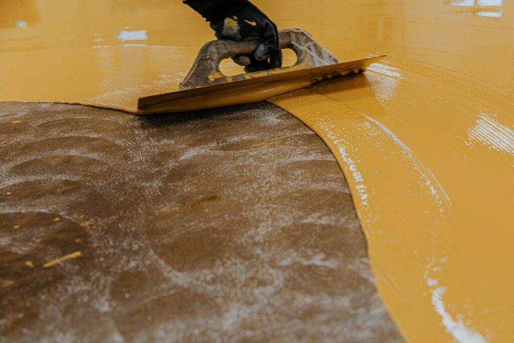 worker, coating floor with self leveling epoxy resin in industrial workshop.